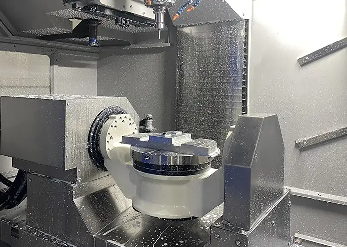 Simultaneous 5-axis CNC milling center in FIWOK Shenzhen workshop, featuring a high-rigidity trunnion rotary table tilting and rotating a custom aluminum block under continuous coolant spray to eliminate datum alignment errors for aerospace parts.